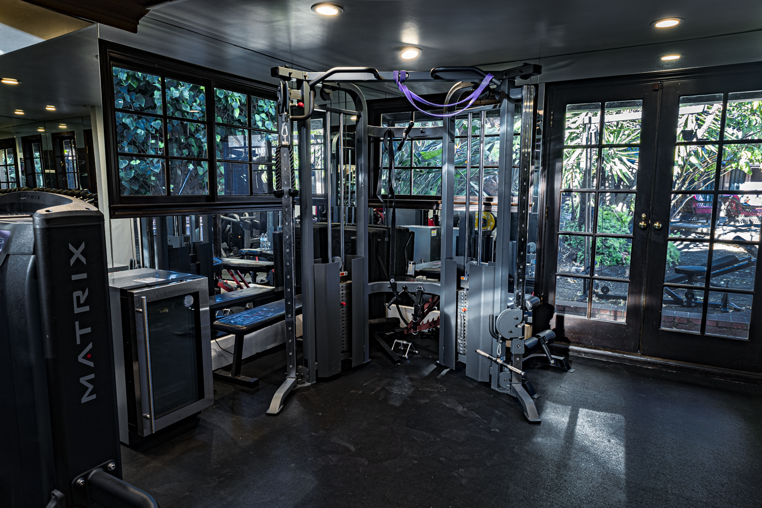 Functional trainer and Matrix machine beside black steel windows and French doors opening to greenery